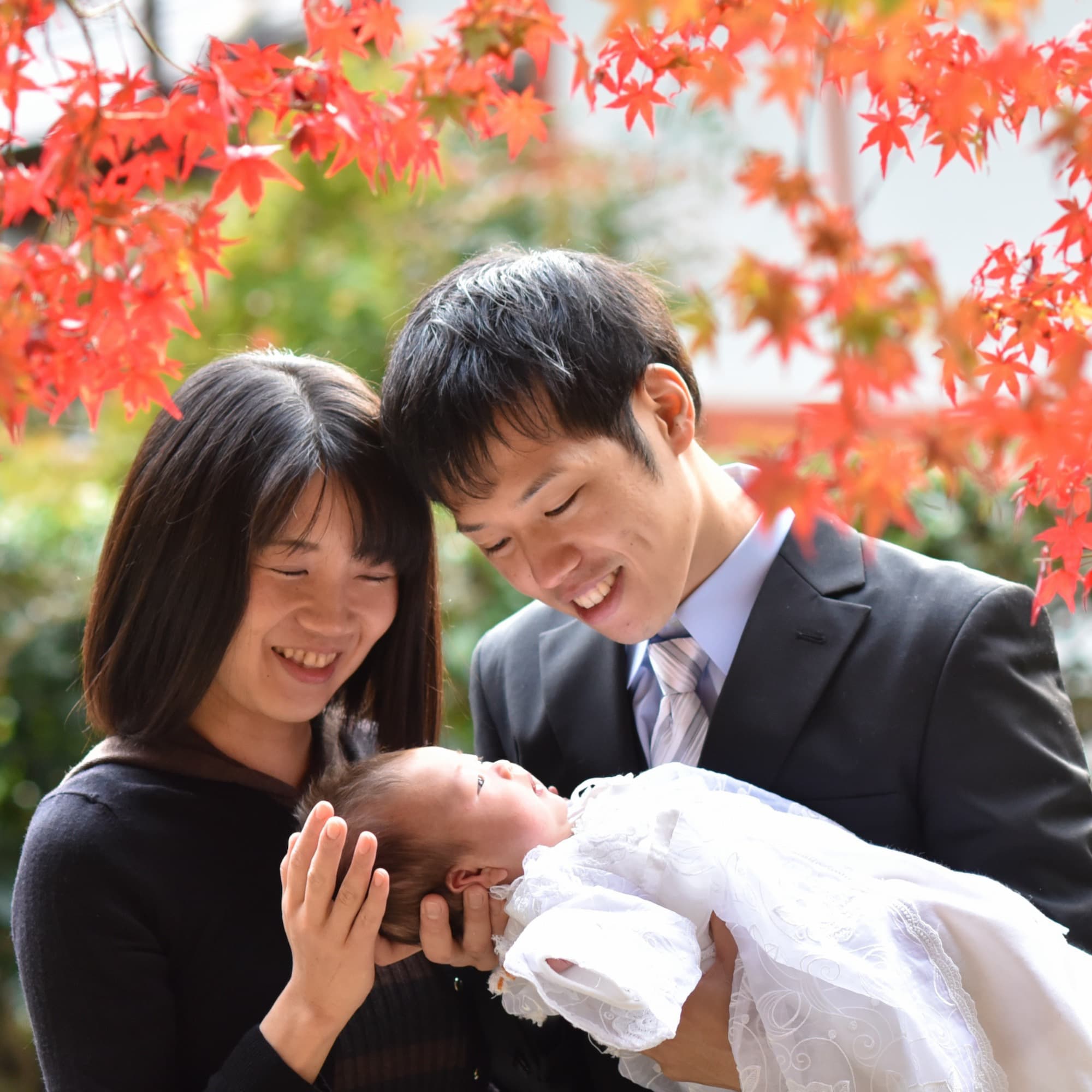 紅葉の下で赤ちゃんを抱いているお父さんとお母さん